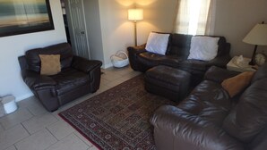 A living room with two leather sofas, a patterned rug, a standing lamp, and a door in the background.
