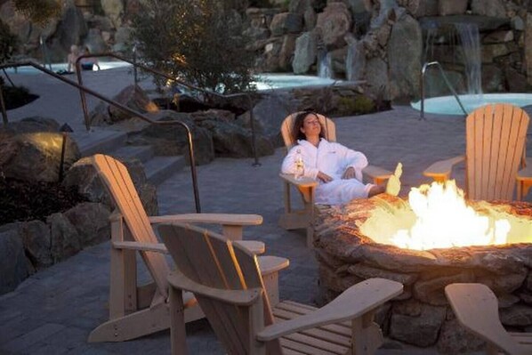 A fire pit with chairs around it, a pool, and a waterfall in the background.