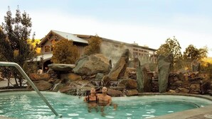 A swimming pool with a waterfall feature, surrounded by large rocks and a building in the background. - Carmel’s HIGHEST RATED and Most ROMANTIC Getaway - Walk to Beach and Town (Carmel)