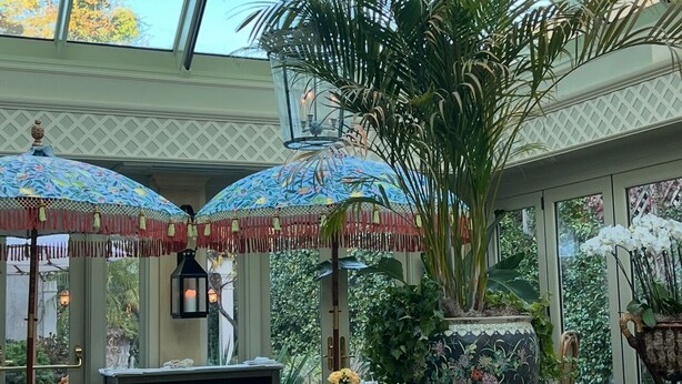 Une véranda dotée d’un toit en verre, de meubles en osier et de plantes en pot.