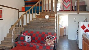 A staircase leading to a loft with a clock, a red and grey patterned sofa, and a kitchen area. - Sherri’s Terlingua Cabin on the Creek: Easy Access (Terlingua)