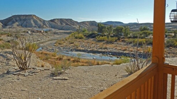 A desert landscape with a gravel path, sparse vegetation, and distant hills. - Sherri’s Terlingua Cabin on the Creek: Easy Access (Terlingua)