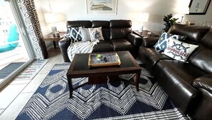 Ein Wohnzimmer mit einem schwarzen Ledersofa, einem Couchtisch, gemusterten Teppichen und einem gerahmten Bild an der Wand.