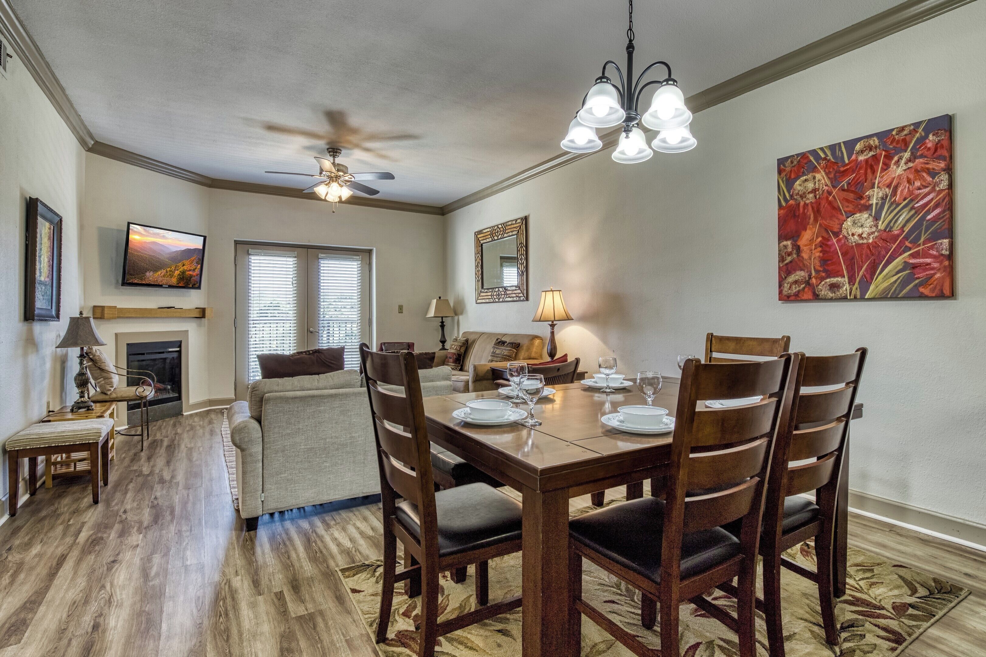 A dining area with a wooden table set for four, a ceiling fan, and a fireplace.