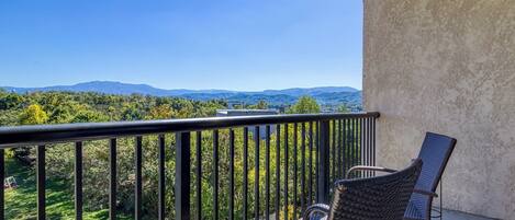 A balcony with wicker chairs, a view of a green landscape and distant mountains.