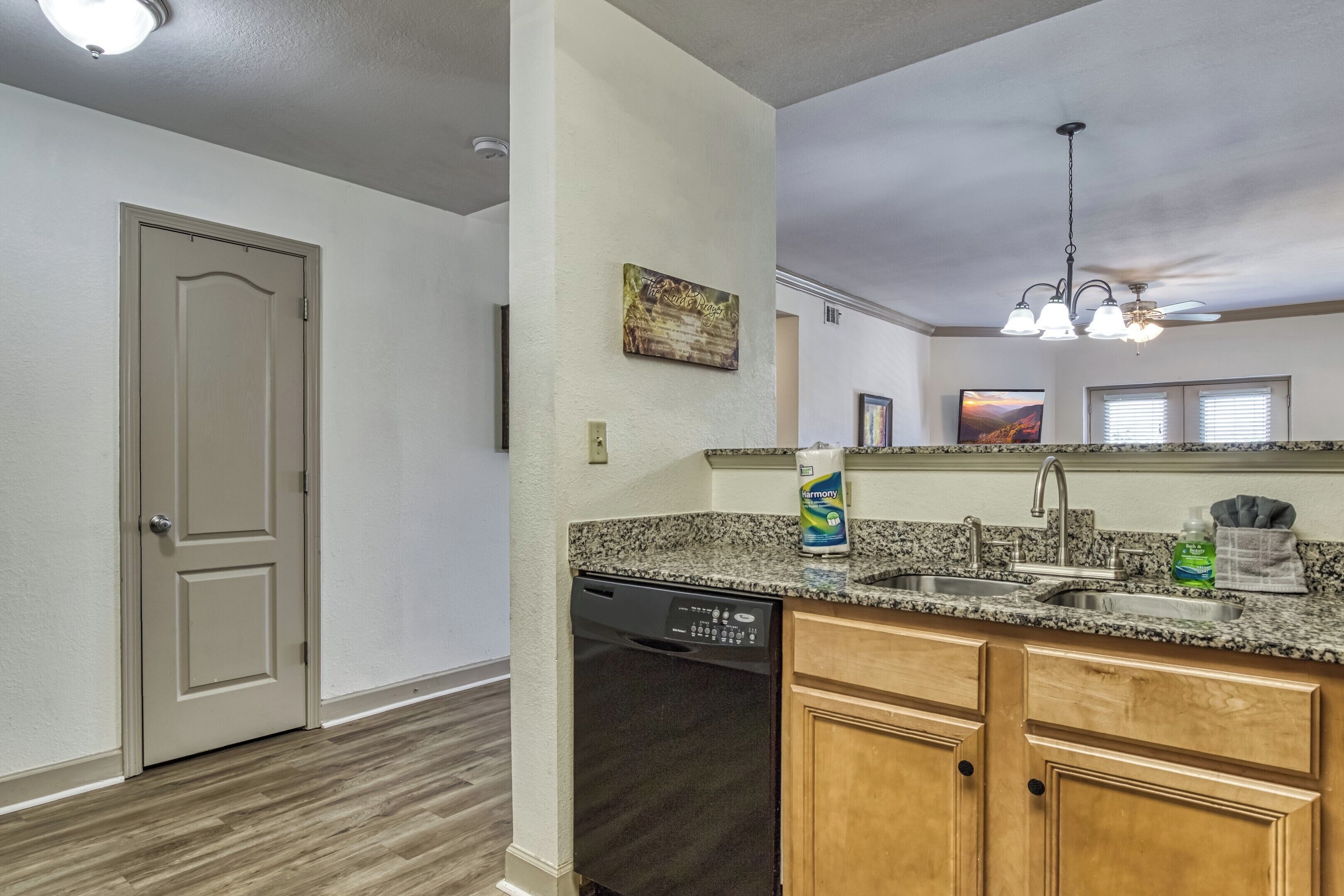 A kitchen with granite countertops, wooden cabinets, a dishwasher, and a ceiling fan.
