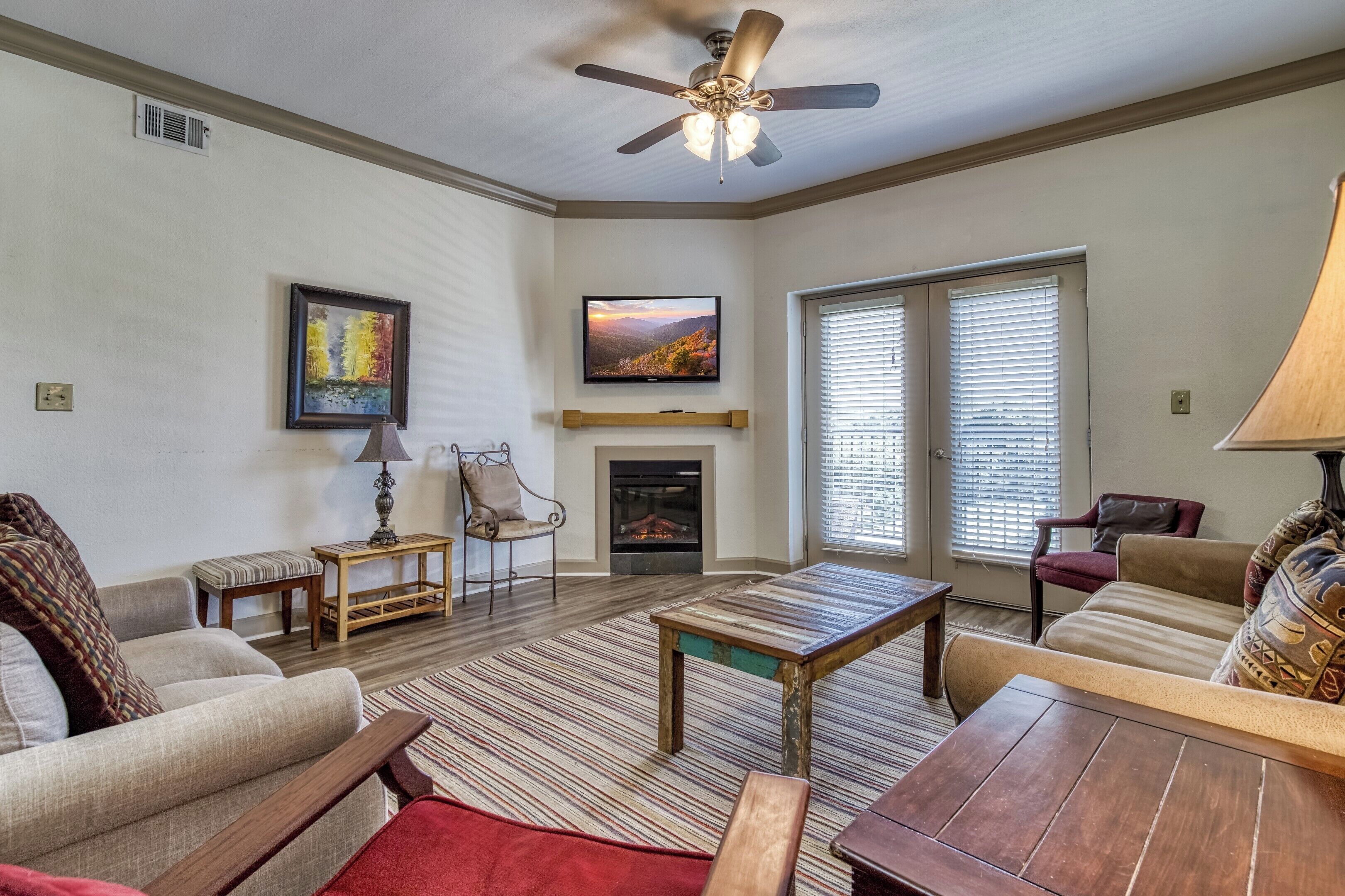 A living room with a fireplace, a ceiling fan, and a television mounted on the wall.