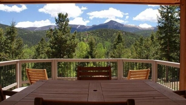 A wooden deck with a table and chairs, overlooking a mountainous landscape with trees and a clear sky. - Altitude with Attitude-Awesome Mountain Cabin  (Divide)