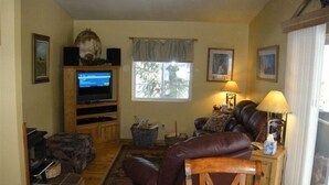 A living room with a television, leather sofa, and a dining table. - Altitude with Attitude-Awesome Mountain Cabin  (Divide)