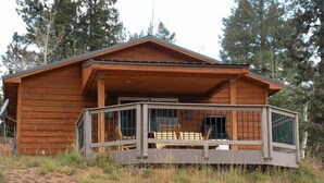 A wooden cabin with a covered porch and a fenced deck area. - Altitude with Attitude-Awesome Mountain Cabin  (Divide)