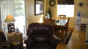 A cozy living room with a leather armchair, a dining table with chairs, a water dispenser, and a ceiling fan. - Altitude with Attitude-Awesome Mountain Cabin  (Divide)