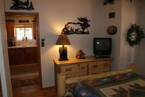 Una camera accogliente con una cassettiera in legno, una lampada, un televisore e un letto con copripiumino.