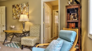 A cozy living room with a patterned armchair, a blue sofa, a wooden side table with a lamp, and a bookshelf filled with books and decorative items. - Single level 4 bdrm w/2 car garage, Golf Course only 200 yrds away!!! (Meridian)