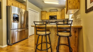 A kitchen with wooden cabinets, a stainless steel refrigerator, a microwave, and two bar stools. - Single level 4 bdrm w/2 car garage, Golf Course only 200 yrds away!!! (Meridian)
