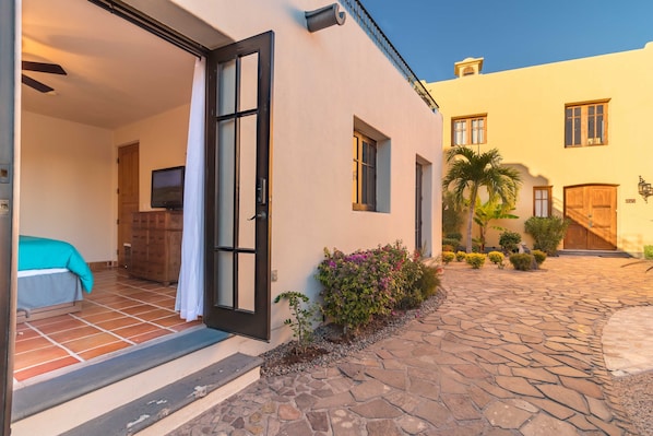 A hotel exterior with a stone-paved courtyard, a wooden door, and a small garden with various plants. - Loreto Bay Poolside Living, Steps from the Beach and Restaurants (Loreto)