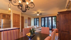 A dining area with a table, chairs, a fruit bowl, a chandelier, and a ceiling fan.