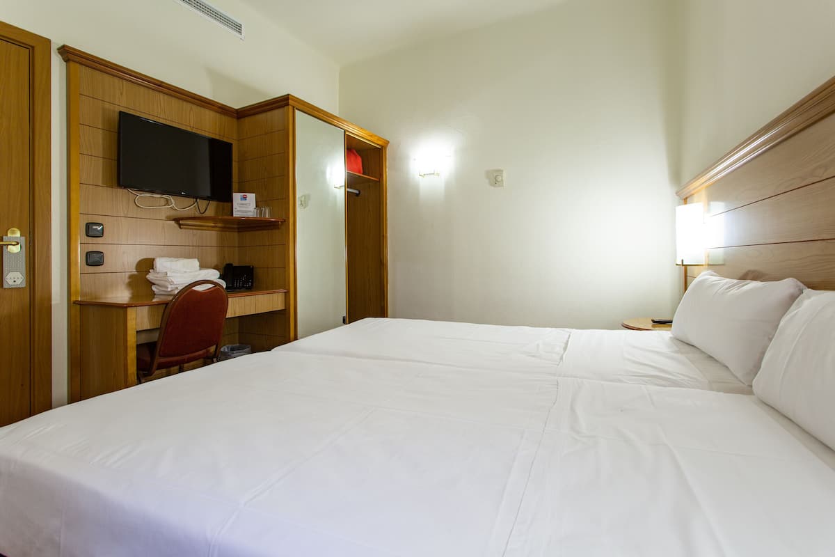 A hotel room with a bed, a desk with a chair, a television, and a nightstand with a lamp.