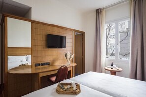 A hotel room with a wooden desk, a flat-screen TV, a bed, and a small table with a bottle and glasses. - Negresco Gran Vía (Madrid)