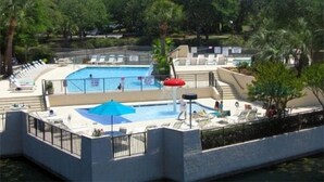 Ein Pool mit Liegestühlen und Sonnenschirmen, umgeben von Bäumen und blauem Himmel.