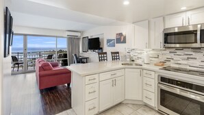 A modern kitchen with white cabinetry, a large island, and a view of the ocean. - Deluxe Waikiki Ocean Front Suite - Ilikai (Honolulu)