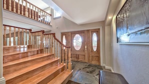 Una escalera de madera con barandilla, suelo de baldosas de piedra y una puerta de madera con paneles de vidrio.