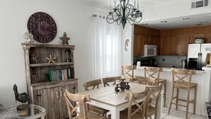 A kitchen with wooden cabinets, a dining table with six chairs, a chandelier, and a large wall clock. - 3BR Duplex ON The Beach, Sleeps 11 Comfortably (Gulf Shores)