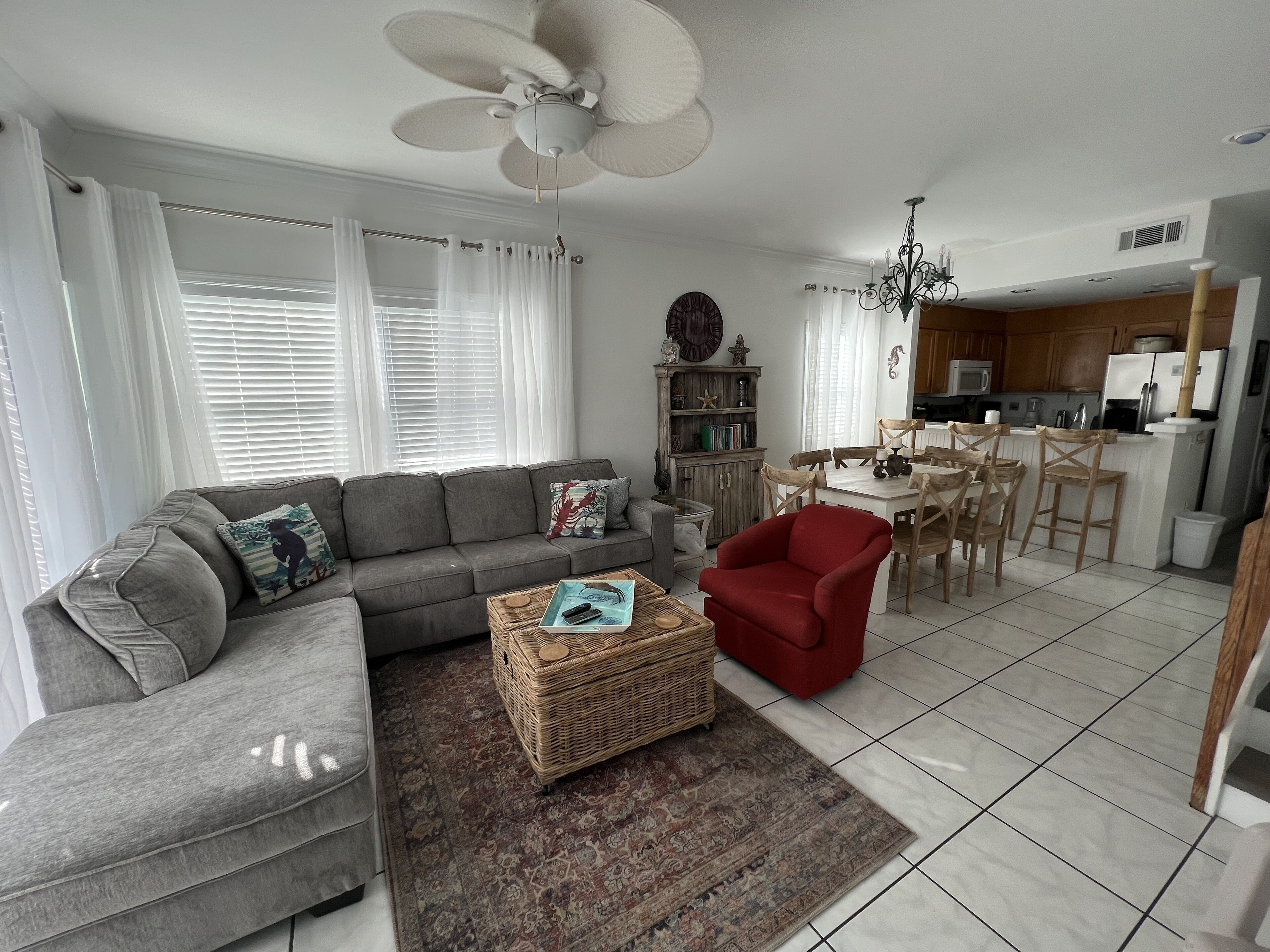 Ein Wohnzimmer mit grauem Sofa, einem roten Sessel, einem Couchtisch und einem Essbereich mit Holzsesseln und einem weißen Tisch.