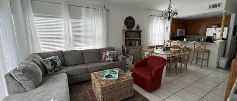 Ein Wohnzimmer mit grauem Sofa, einem roten Sessel, einem Couchtisch und einem Essbereich mit Holzsesseln und einem weißen Tisch.