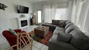 A living room with a fireplace, a sofa, a red chair, a television, and a ceiling fan. - 3BR Duplex ON The Beach, Sleeps 11 Comfortably (Gulf Shores)