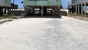 A two-story beachfront house with a sandy ground floor and a wooden deck. - 3BR Duplex ON The Beach, Sleeps 11 Comfortably (Gulf Shores)