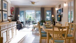 A spacious living area with a dining table, chairs, and a sofa. There is a kitchen area with cabinets and a countertop. The room has large windows and curtains. - Bijou! Sophistication and comfort in Turtle Cove (Providenciales)