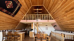 Une chambre spacieuse située sous les combles, avec un espace repas surélevé, un plancher en bois et un escalier menant à l’étage supérieur.