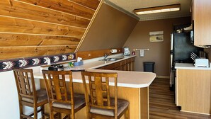 Une cuisine avec des meubles de rangement en bois, un plan de travail et un coin bar avec des tabourets.
