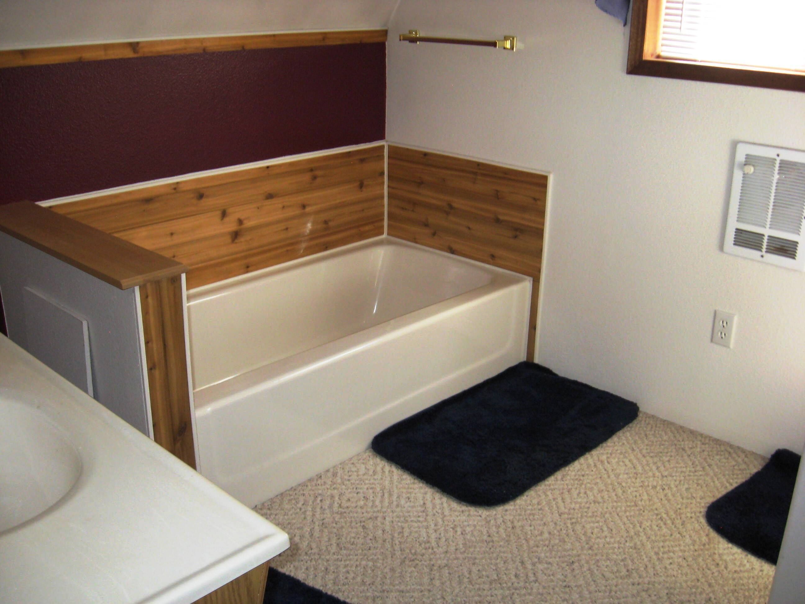 A small bathroom with a wooden vanity, a bathtub, and a carpeted floor.