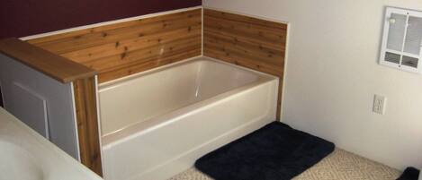 A small bathroom with a wooden vanity, a bathtub, and a carpeted floor.