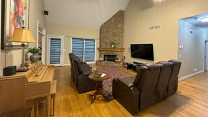 A spacious living room with a fireplace, a flat-screen TV, and a ceiling fan.
