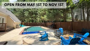 A backyard with a swimming pool, deck chairs, and a wooden fence.