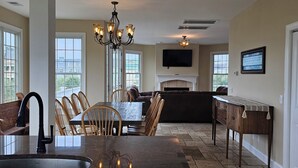 A spacious kitchen with a central island, a dining area with chairs, a fireplace, and a TV mounted on the wall. - So Close to the Beach & Pool! (Pawleys Island)
