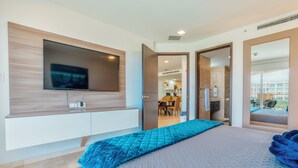 Un dormitorio moderno con una cama grande, un televisor montado en la pared y vistas a la cocina y al balcón a través de una puerta abierta.