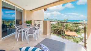 Un balcón con zona de comedor, sofá y vistas al océano y palmeras.