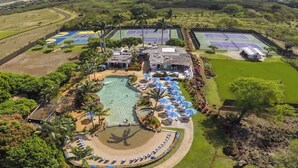 Oversigtsbillede af et resort med swimmingpool, tennisbaner og en anlagt have med parasoller.
