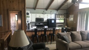 Una sala de estar acogedora con un sofá, una lámpara y una mesa de centro. Cuenta con una zona de cocina equipada con refrigerador, microondas y alacenas.