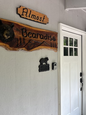 A wooden sign with 'Almost Paradise' and a bear carving, a welcome sign, and a door with a window.
