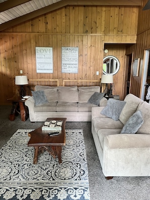 A cozy living room with a wooden ceiling, two couches, a coffee table, and a patterned rug.