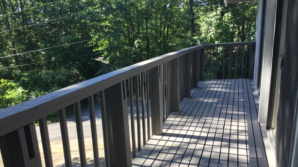 Una terraza de madera con barandilla de metal, rodeada de árboles.