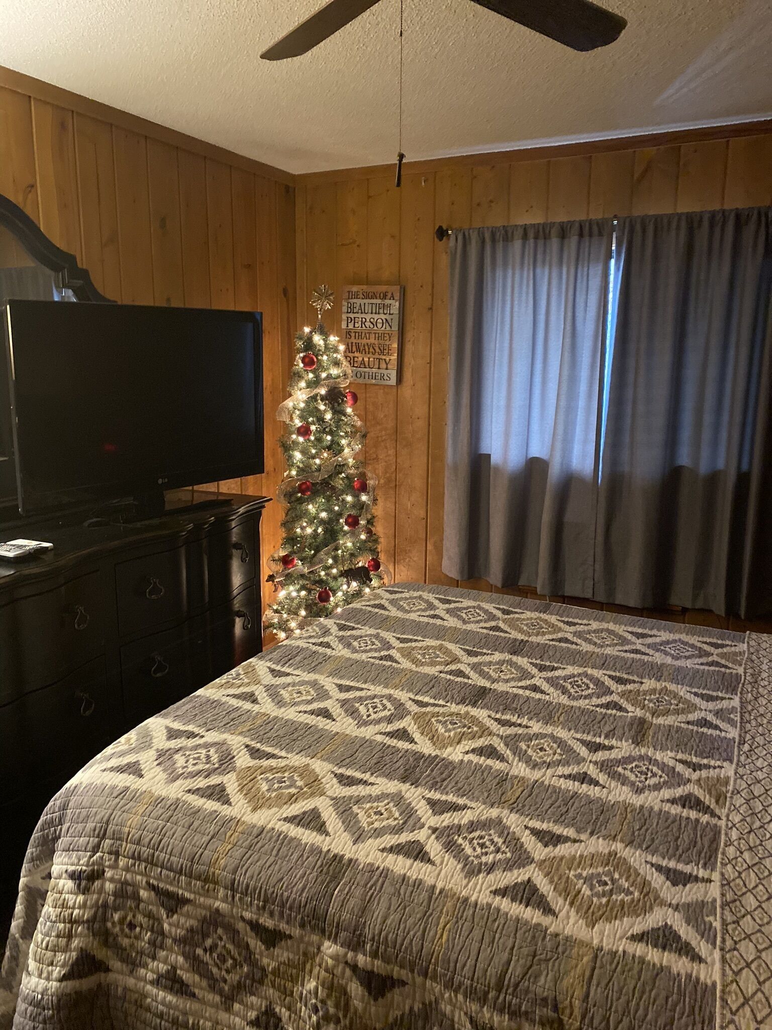 Un dormitorio con cama, cómoda, televisor, árbol de Navidad y ventilador de techo.
