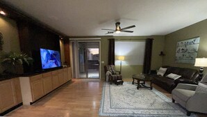 Ett vardagsrum med en tv, en takfläkt, en soffa, ett soffbord och en matta.