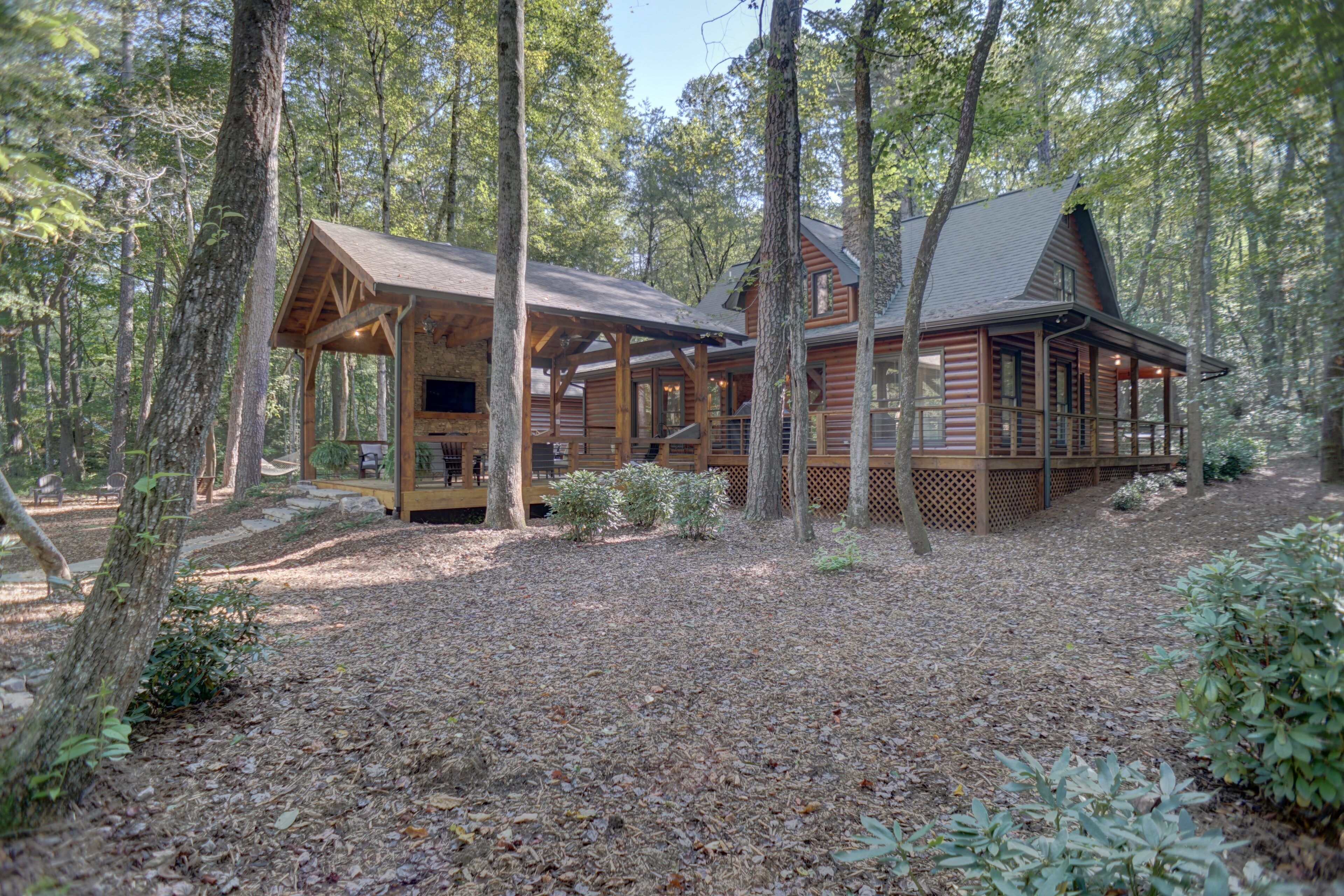 A cabin with a covered porch and a deck, surrounded by trees in a wooded area.
