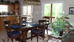 Uma sala de jantar com mesa e cadeiras de madeira, um candelabro e uma janela ampla com vista para o verde.