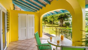 Una habitación amarilla con balcón, una mesa con dos vasos de zumo de naranja y una silla verde.